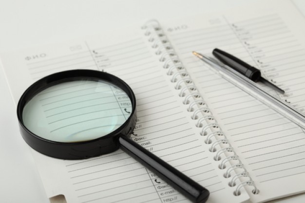 magnifying-glass–white-background–sheets–opened-notebook_3207297